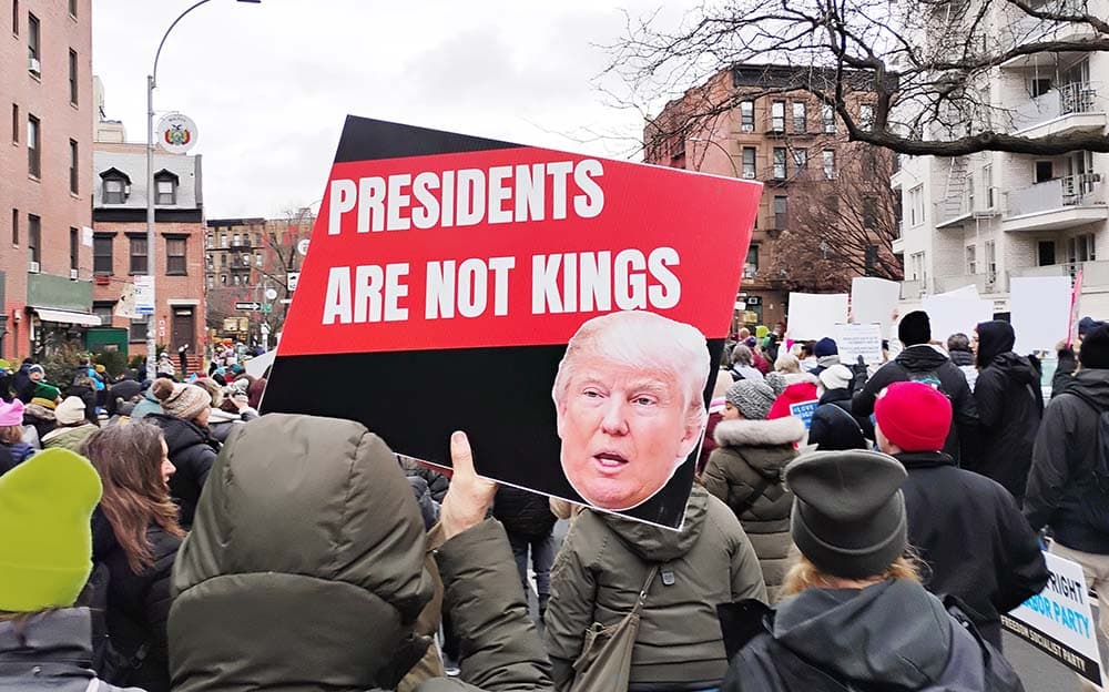 Protester holds sign reading 'Presidents Are Not Kings' at demonstration in urban street