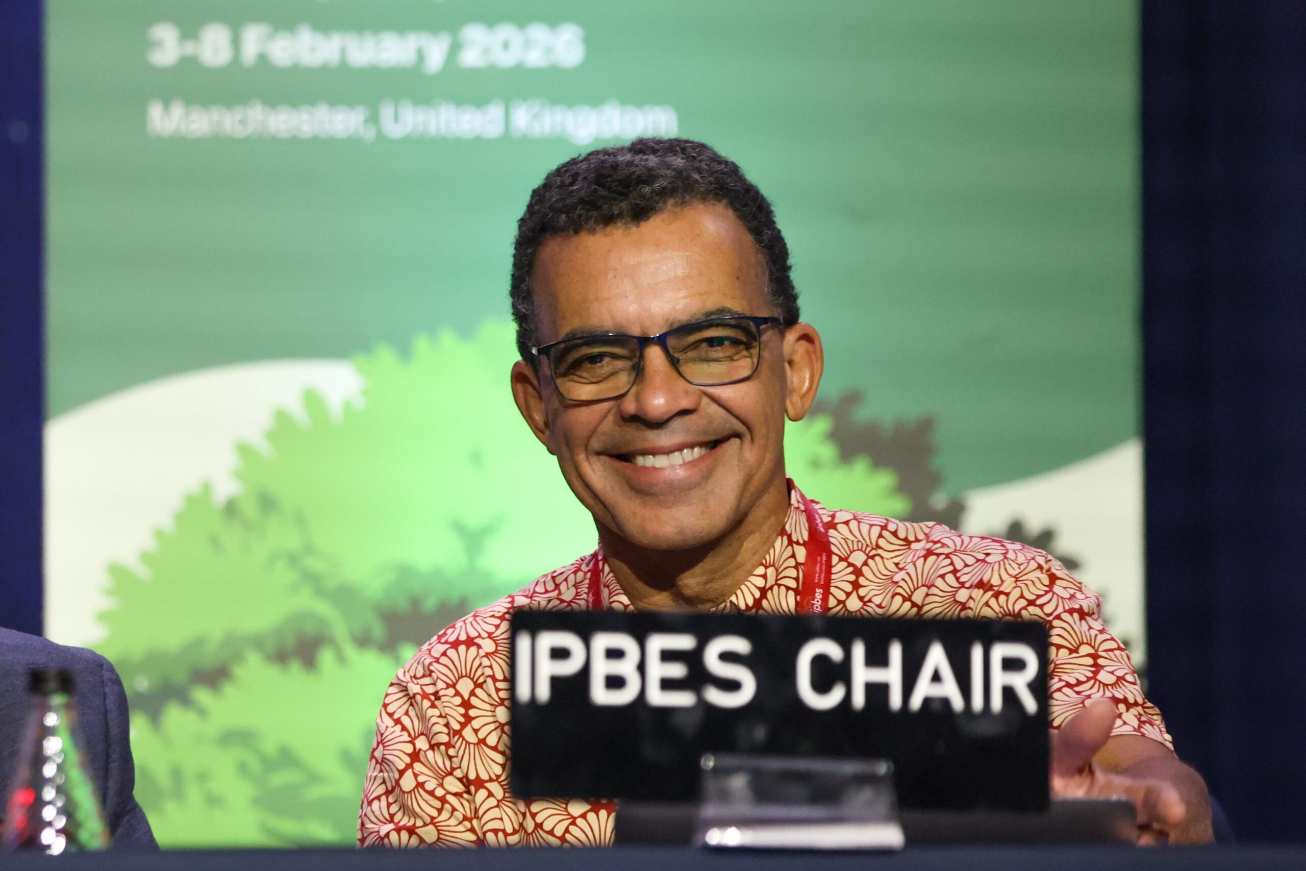IPBES Chair at the Manchester plenary session with nameplate and presentation screen showing February 2026 date