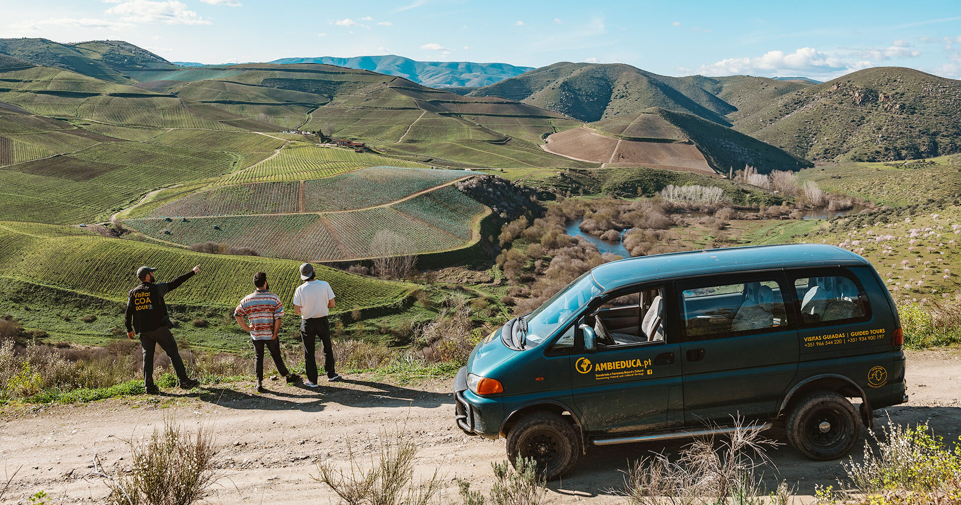 Three people view terraced vineyards and rolling hills in Portugal's Greater Côa Valley from a dirt road