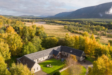 Aerial view of Ballintean Mountain Lodge courtyard surrounded by autumn forest and Highland mountains