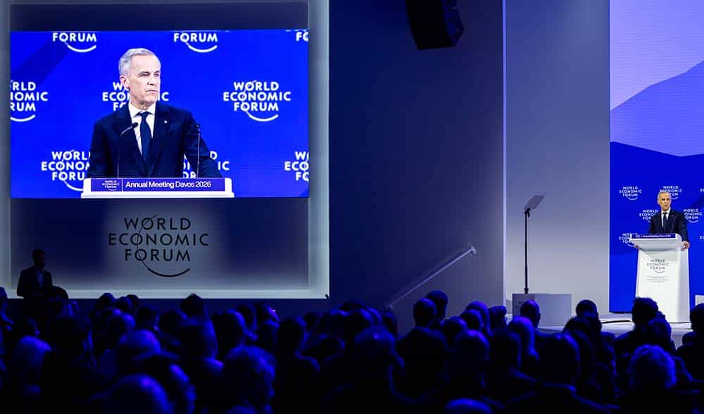 Speaker at World Economic Forum Davos podium addressing audience, blue branding visible