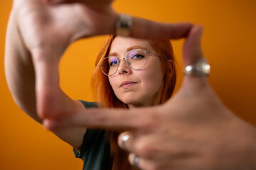 Photographer framing shot with hands, woman with glasses centered through finger frame