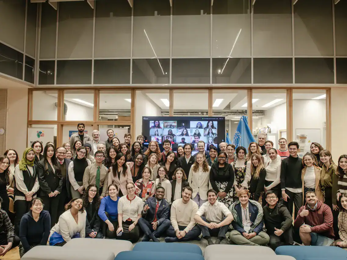 Large diverse group of young participants gathered for UN Youth Compass dialogue with virtual attendees on screen